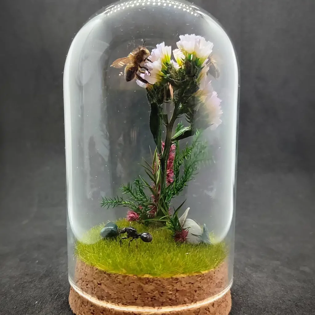 Cloche entomologique avec diorama montrant une gyne de fourmis Messor barbarus et des abeilles Apis mellifera, décoré de fleurs, de végétaux et de pierres d'agate indienne.