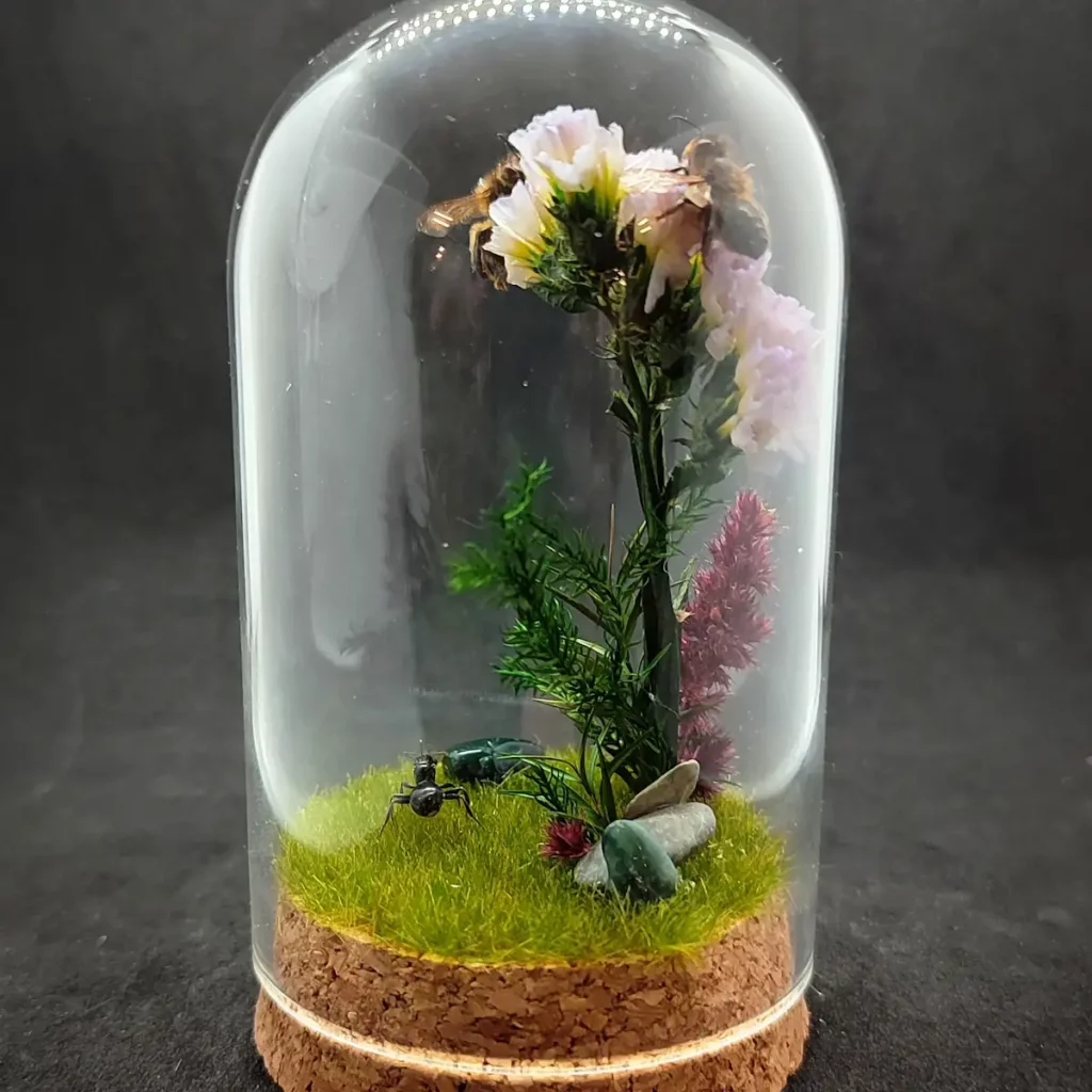 Cloche entomologique avec diorama montrant une gyne de fourmis Messor barbarus et des abeilles Apis mellifera, décoré de fleurs, de végétaux et de pierres d'agate indienne.