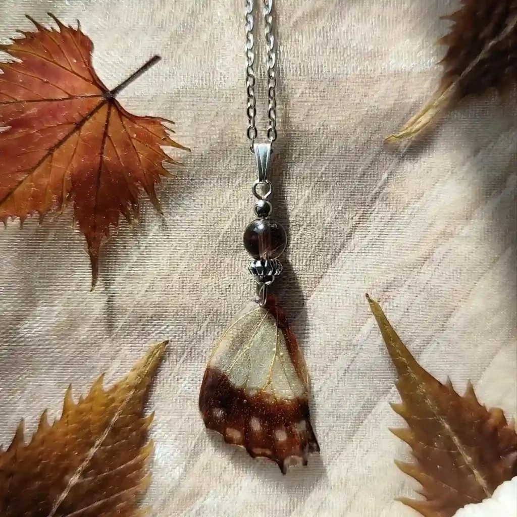 Collier avec pendentif en résine contenant une aile de papillon Graphium angolanus et du quartz fumé.