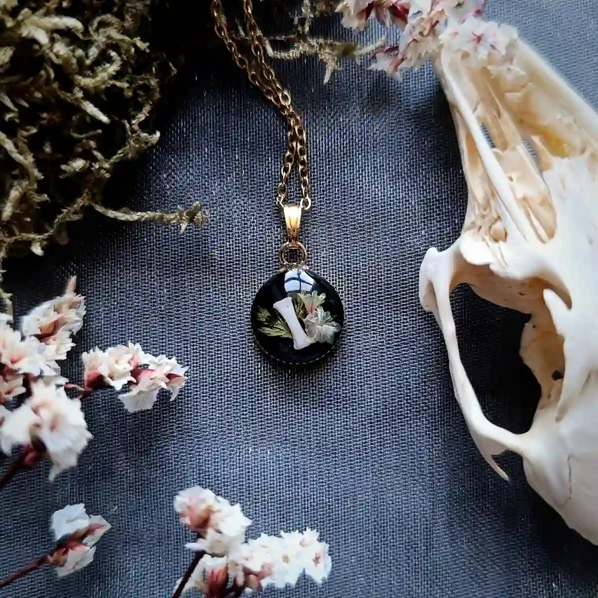 Collier en acier inoxydable avec pendentif en résine contenant un os de lapin et des fleurs et végétaux.