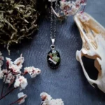 Collier en acier inoxydable avec pendentif en résine contenant un os de lapin et des fleurs et végétaux.