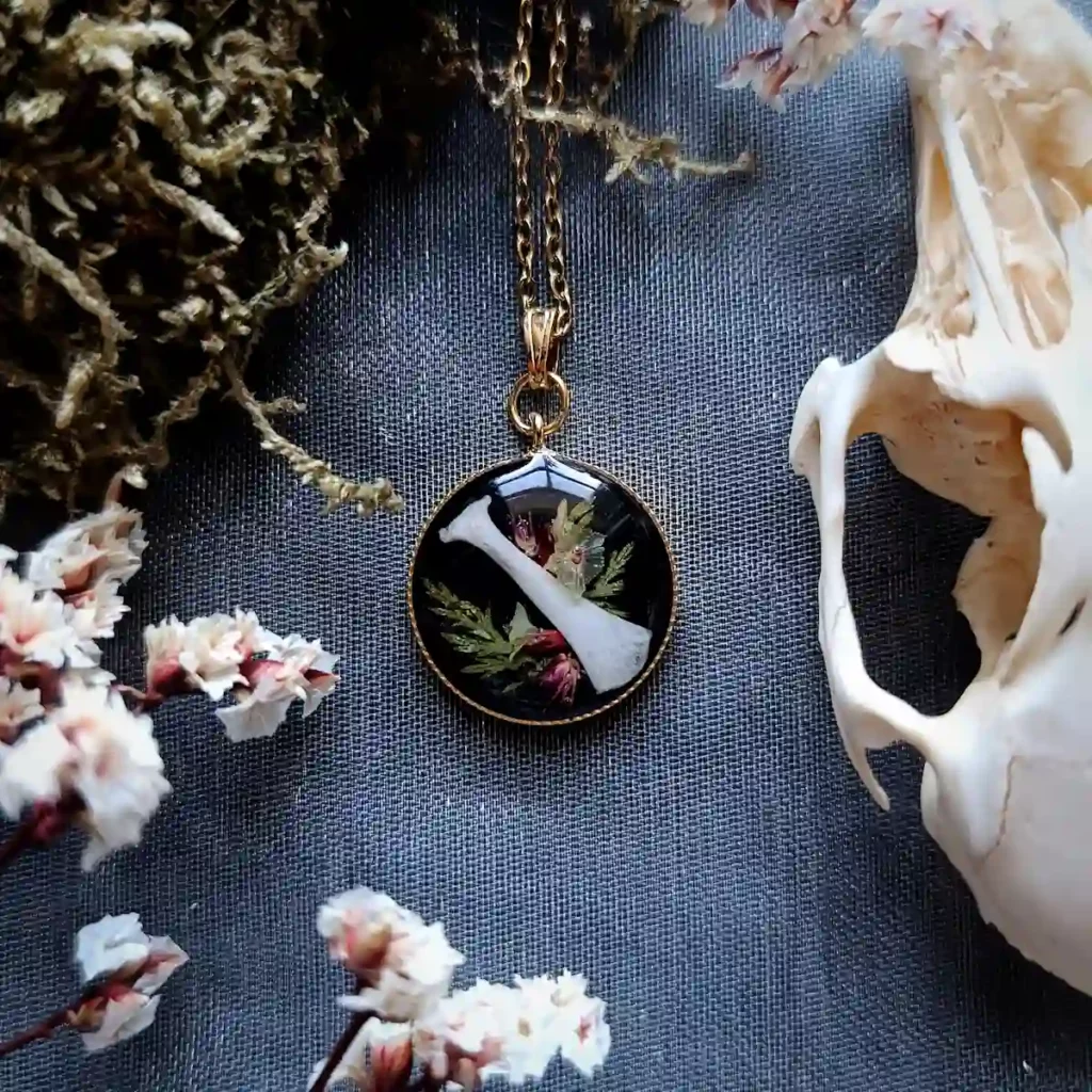 Collier en acier inoxydable avec pendentif en forme d'os de lapin, inclus dans de la résine avec des fleurs et des végétaux.