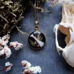 Collier en acier inoxydable avec pendentif en forme d'os de lapin, inclus dans de la résine avec des fleurs et des végétaux.