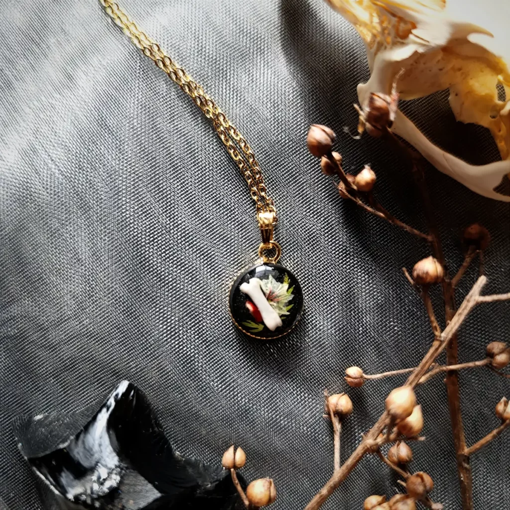 Collier discret avec pendentif en résine contenant un os et des fleurs.